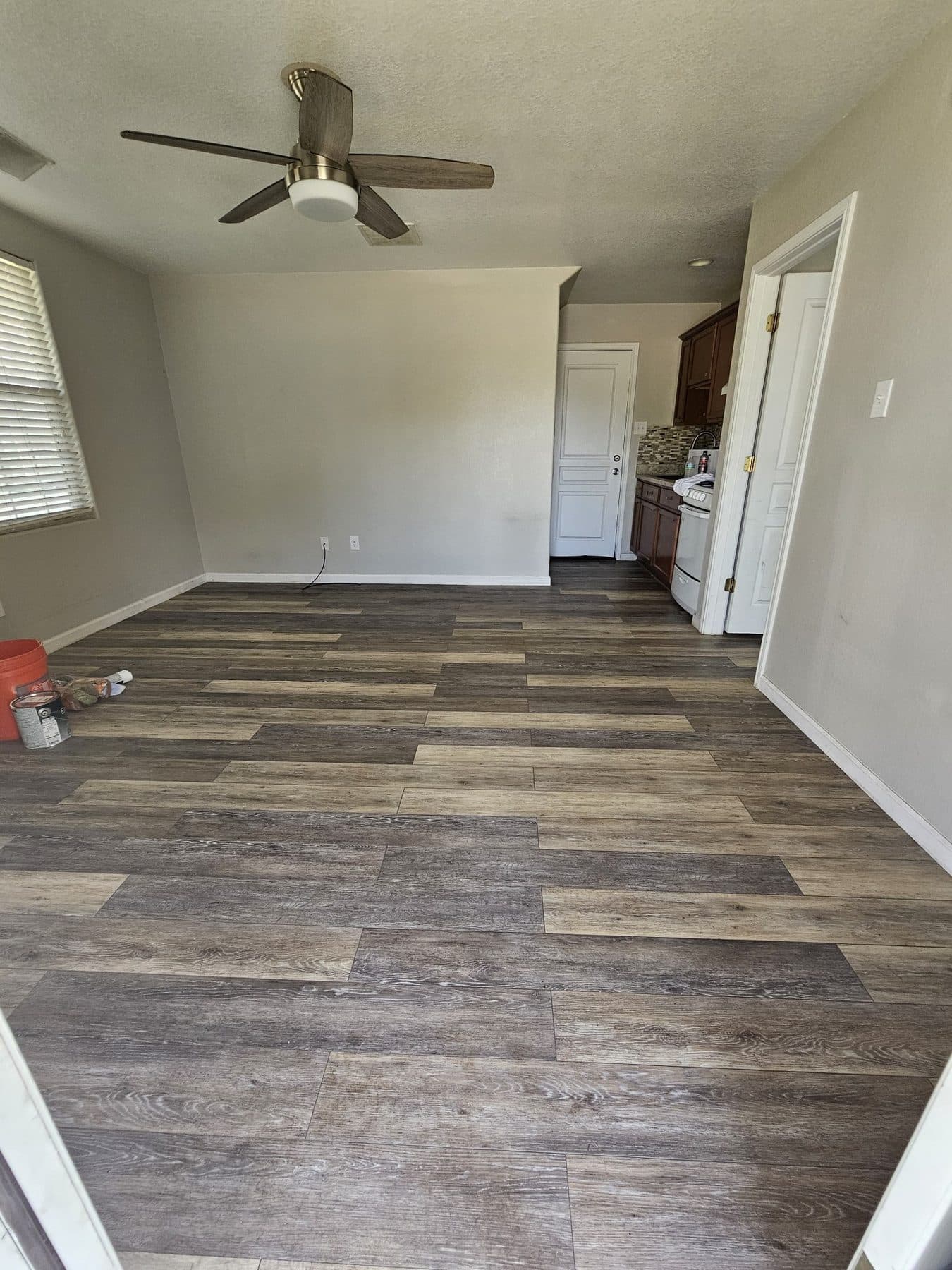 Living room with newly installed wide wood-look plank flooring running toward a kitchen