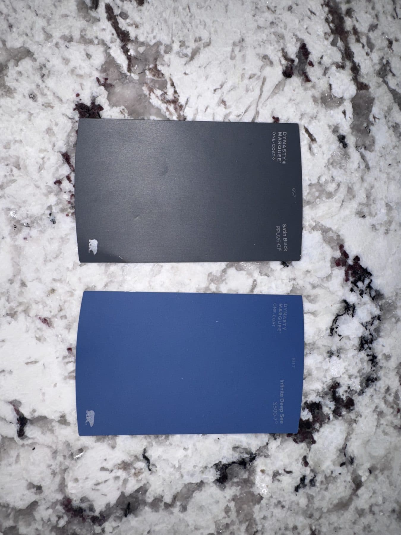 Two large paint colour sample cards laid out on a granite countertop