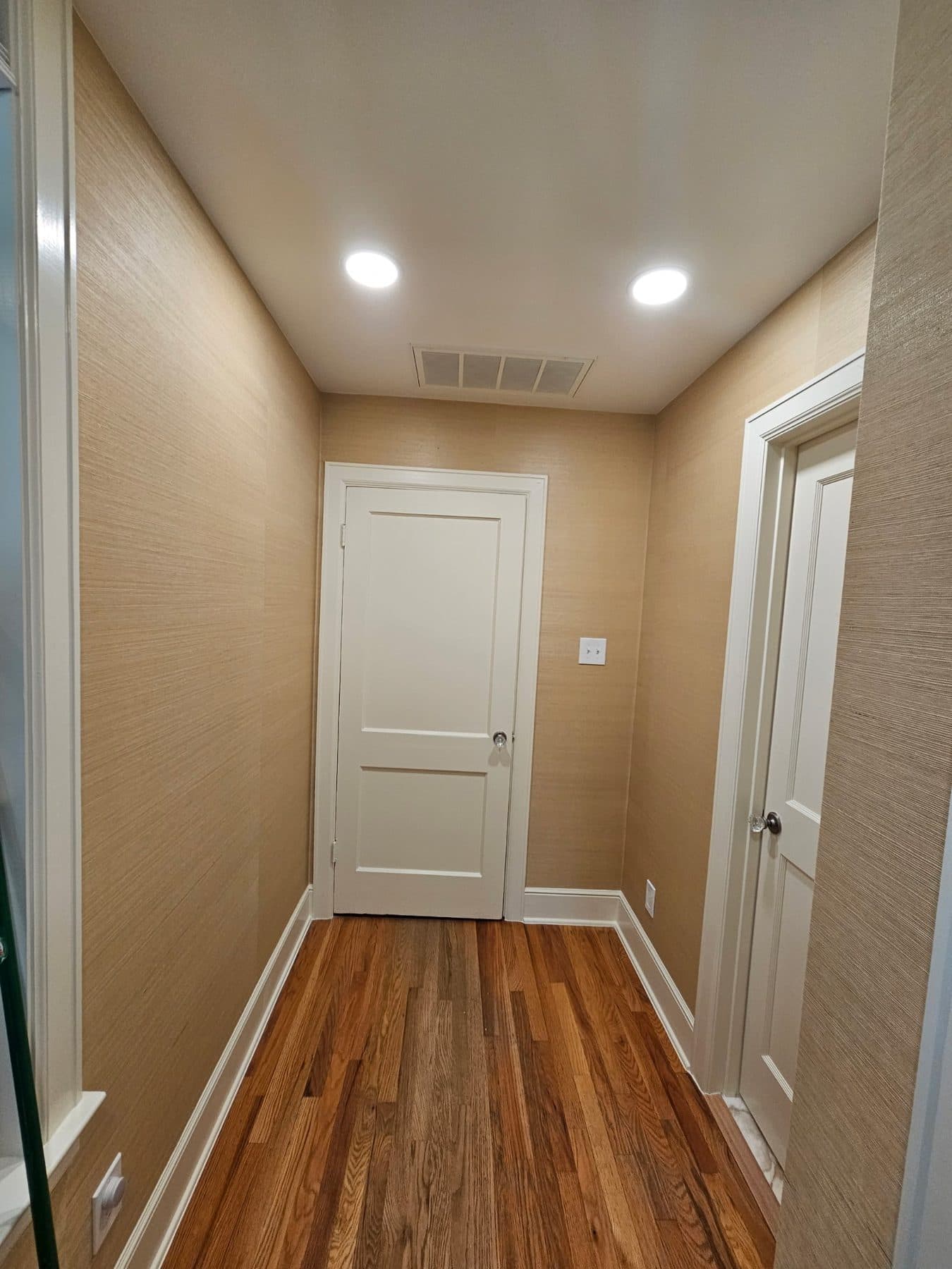 Finished hallway with warm painted walls, white door and hardwood flooring