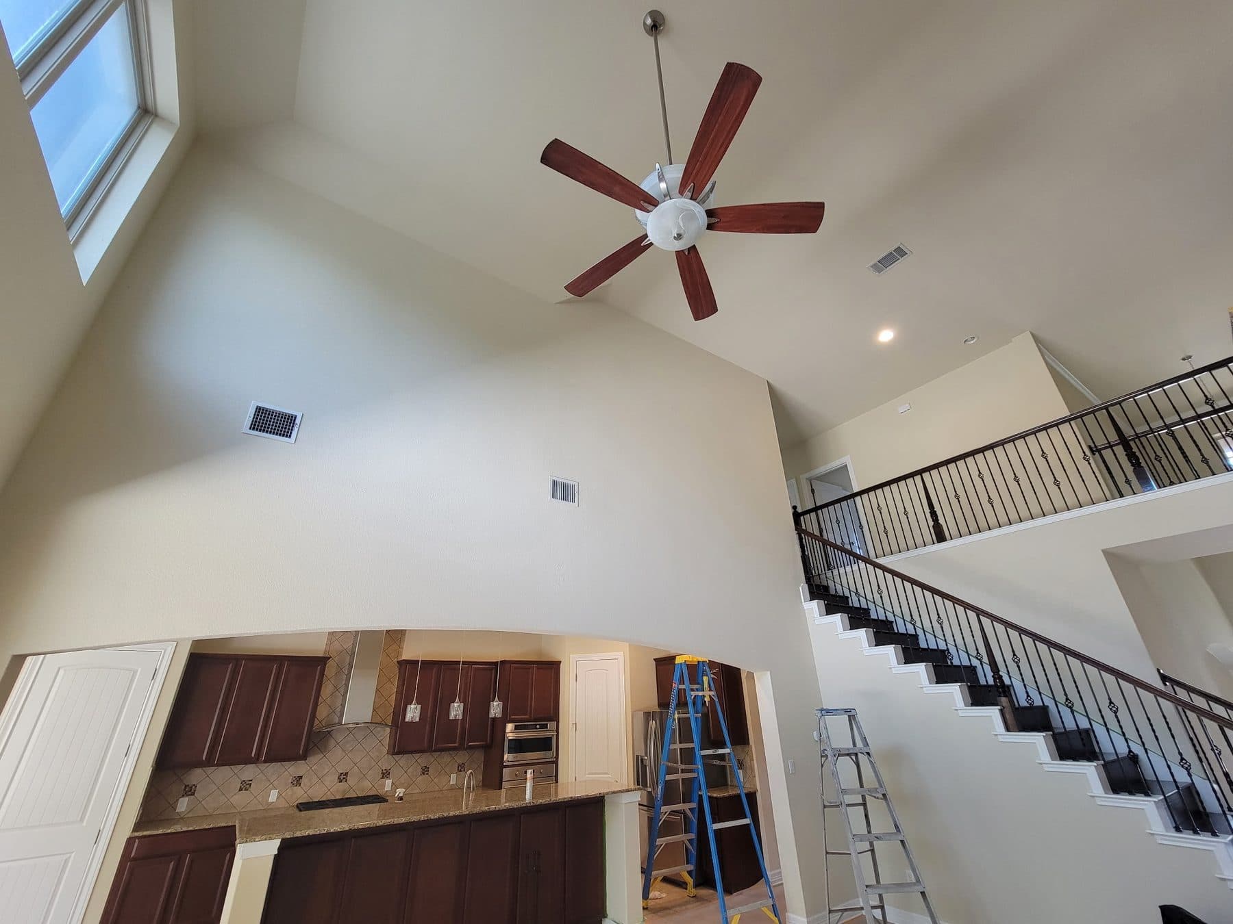 Vaulted ceiling living area with ladders set up and surfaces protected during painting